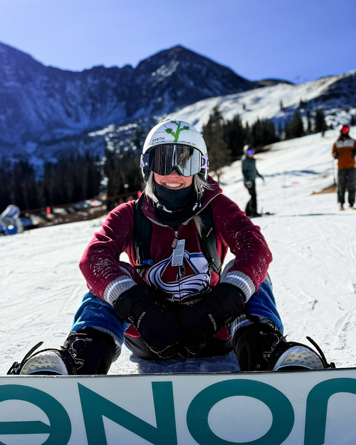 Bri sitting on her snowboard on a mountain slope, smiling