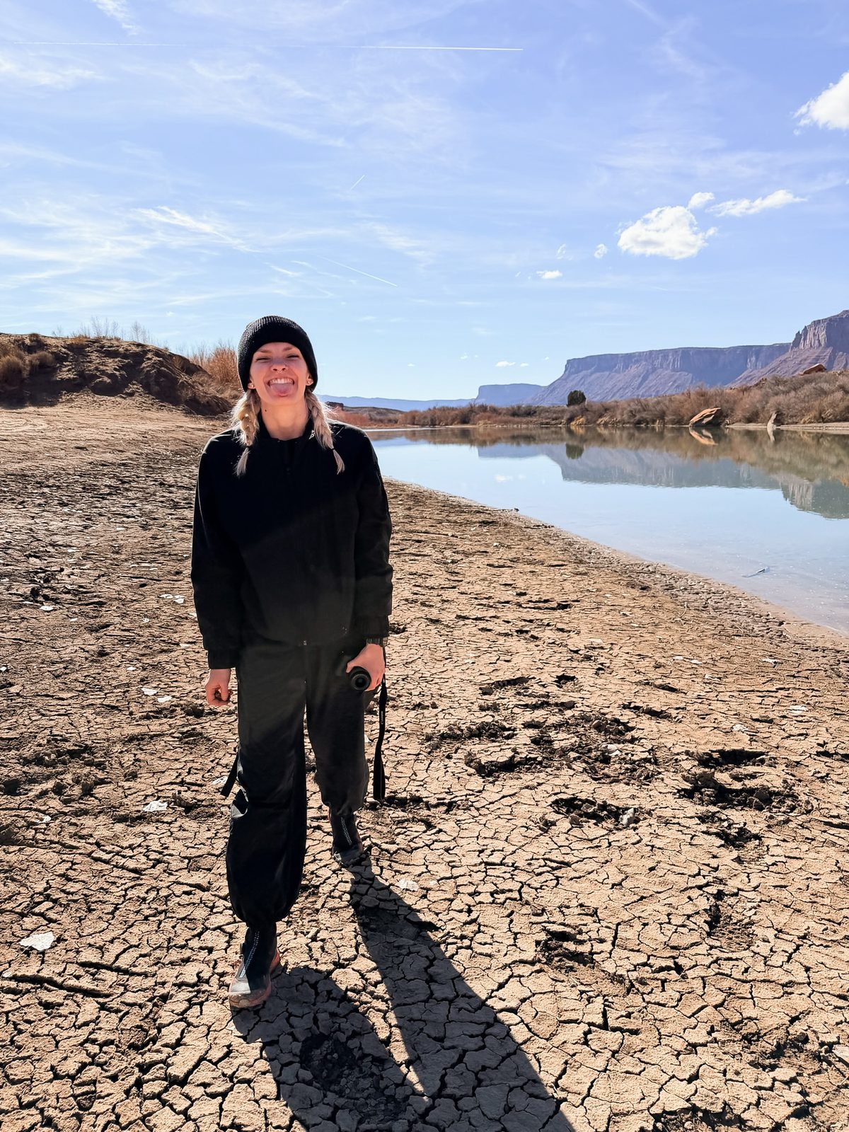 Bri standing on cracked mud flats next to a river with red rock cliffs behind her
